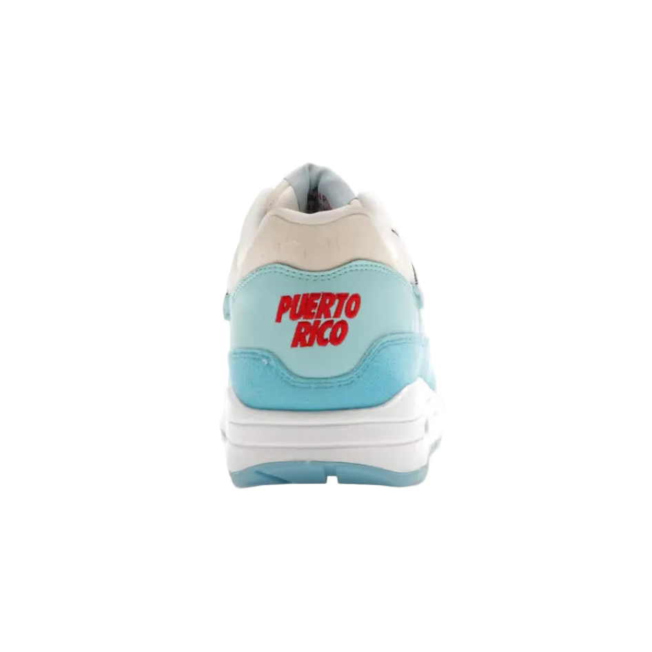 A single sneaker shown from the back on a plain white background, with a small horizontal slider line below it. The shoe has a white and light blue design with red 'PUERTO RICO' text on the heel.