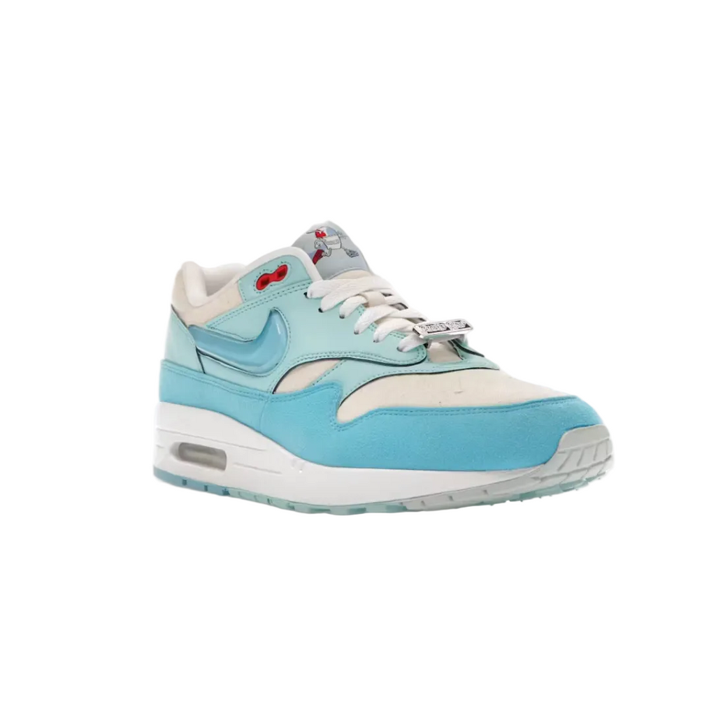 A Nike Air Max 1 sneaker in light blue suede and cream leather, featuring a light blue Swoosh and a small red bow detail on the tongue, shown against a plain white background.