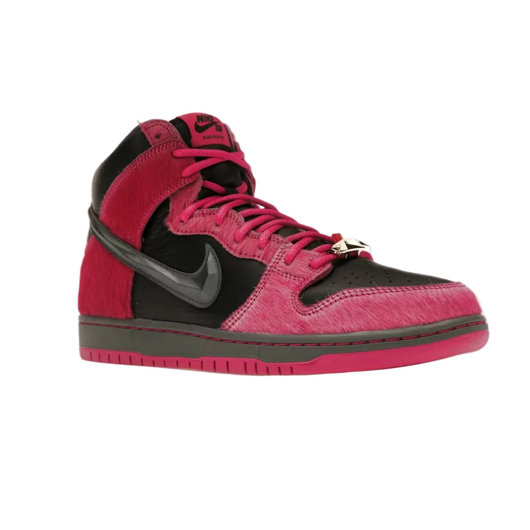 A Nike high-top sneaker in vibrant pink and black suede, featuring a metallic gray Swoosh and a small gold ring detail on the laces, set against a plain white background.